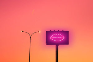 Billboard with sexy lips neon light and sunset sky in the city.